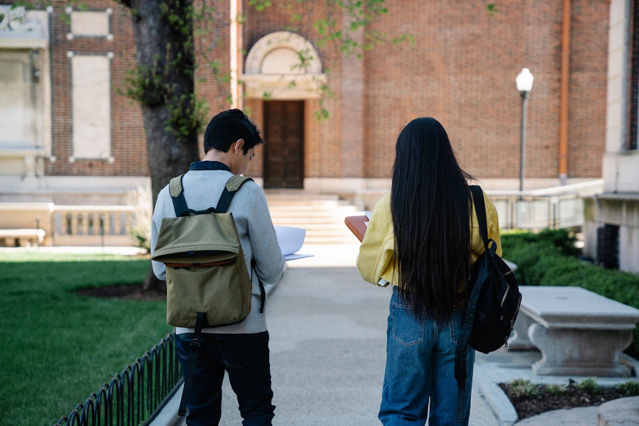 Two college students with backpacks walking near a university building.